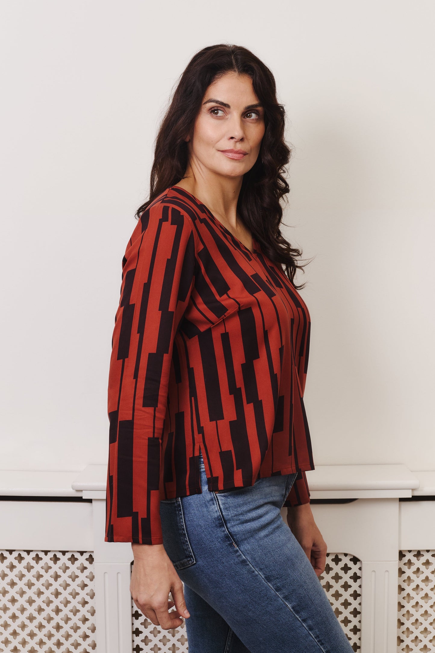 Side view of woman, model wearing v neck rust coloured long sleeved top. Model is fuller bust size. Fabric is 100% LENZING™ ECOVERO™ Viscose. A drapey fabric isoft with a simple, large scale geometric print.