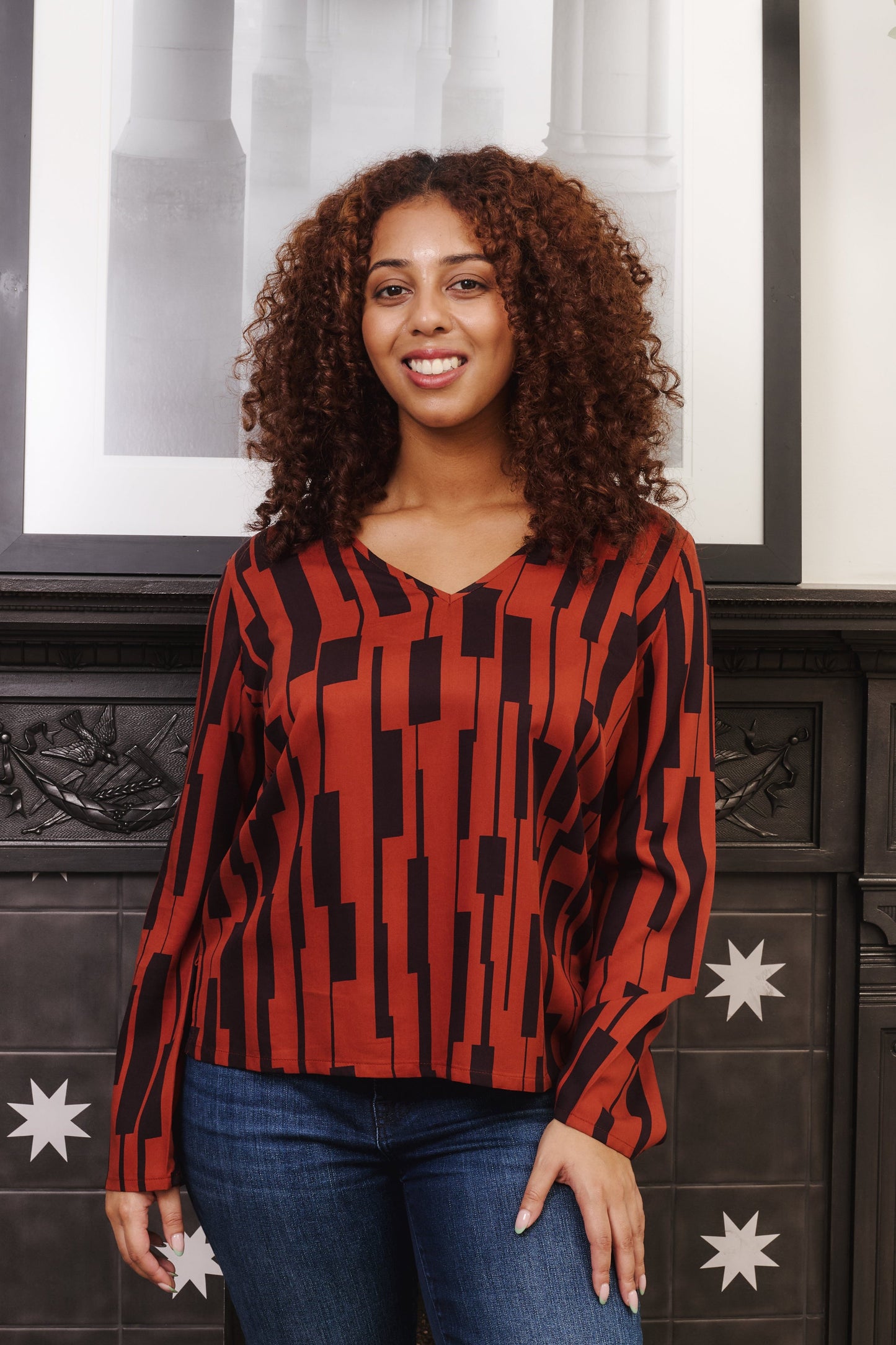 Model wearing v neck rust coloured long sleeved top. Model is fuller bust size. Fabric is 100% LENZING™ ECOVERO™ Viscose. A drapey fabric isoft with a simple, large scale geometric print.