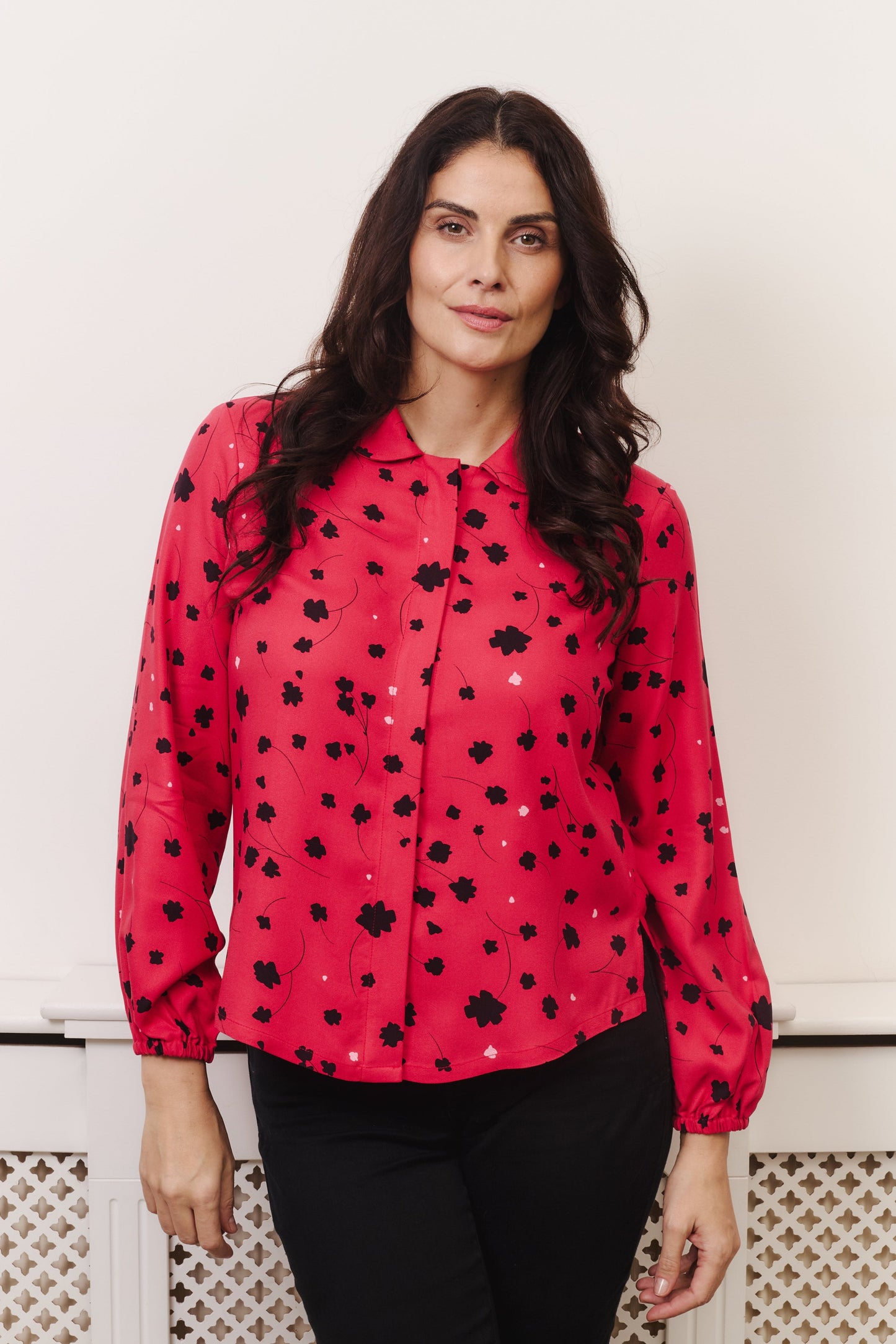 Model wears vibrant crimson coloured blouse, with hidden button, rounded collar and elasticated cuffs. Fabric is 100% LENZING™ ECOVERO™ Viscose - which has a lightly crisp touch with a soft fluid drape. Its fully opaque and has a soft semi-matte sheen.