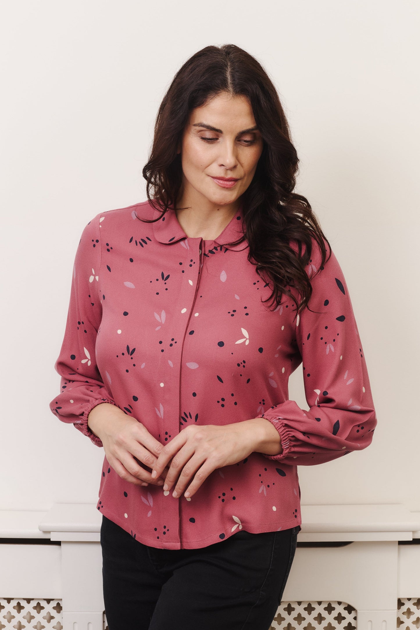 Model with fuller bust wears rose coloured blouse, with hidden button, rounded collar and elasticated cuffs. Fabric is 100% LENZING™ ECOVERO™ Viscose - which has a lightly crisp touch with a soft fluid drape. Its fully opaque and has a soft semi-matte sheen.