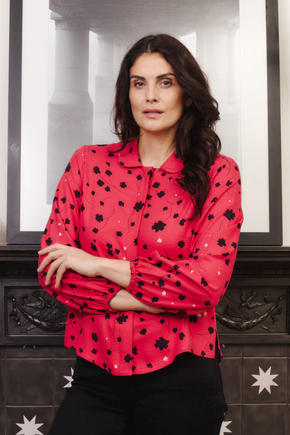 Model with fuller bust wears vibrant crimson coloured blouse, with hidden button, rounded collar and elasticated cuffs. Fabric is 100% LENZING™ ECOVERO™ Viscose - which has a lightly crisp touch with a soft fluid drape. Its fully opaque and has a soft semi-matte sheen.